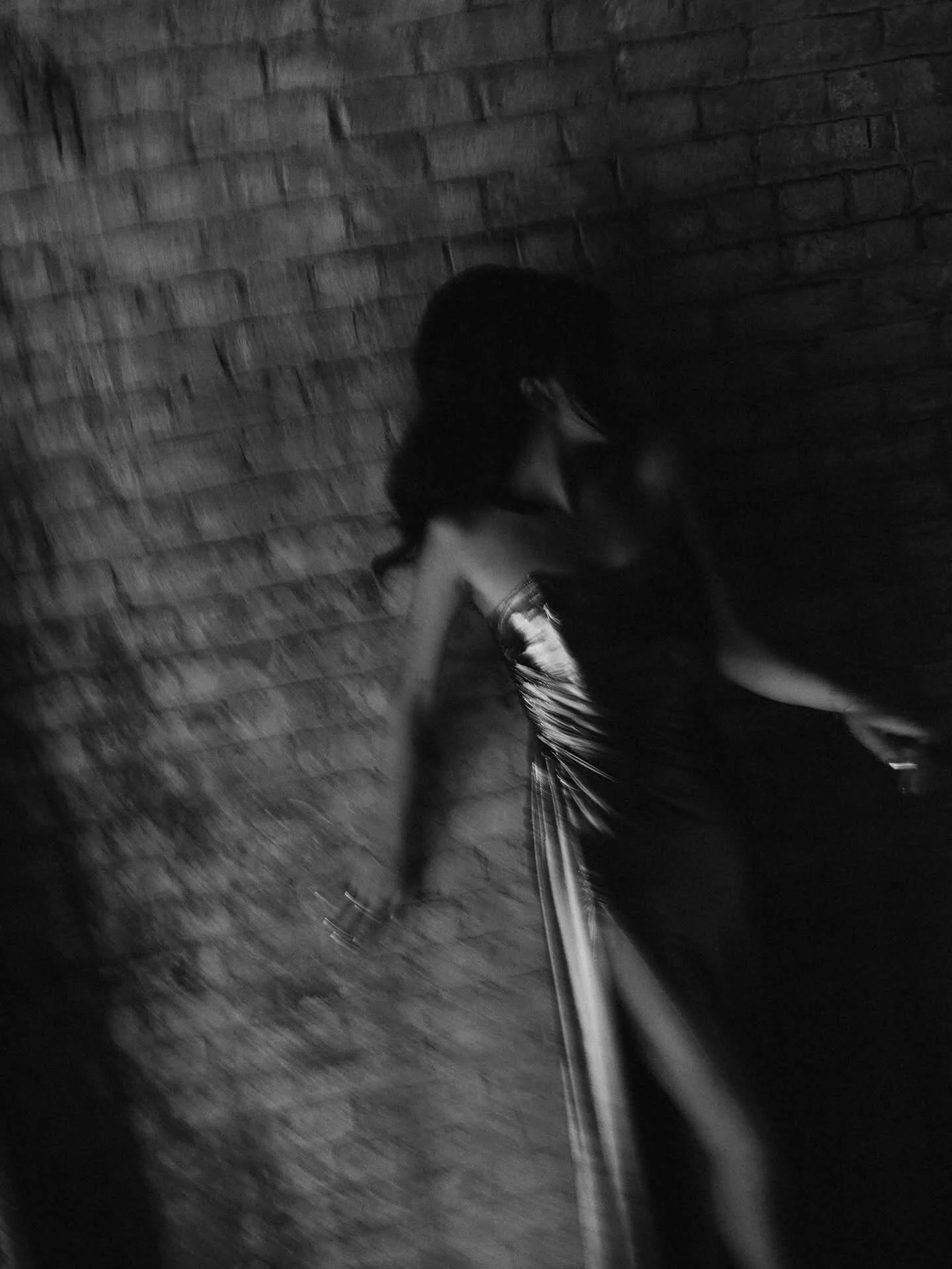 Dark black-and-white figure study against brick