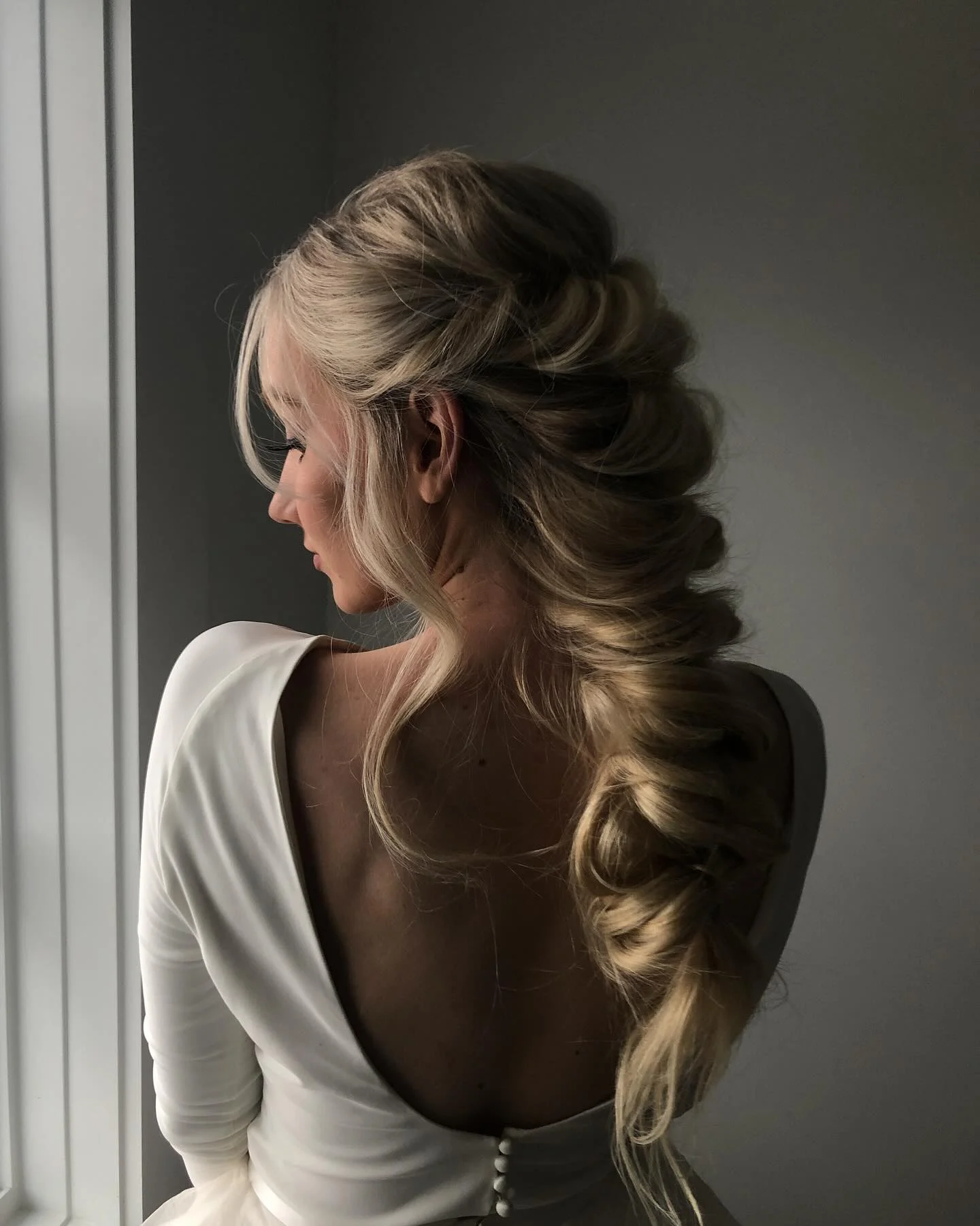 Editorial bridal profile with sculpted hair and a warm cream backdrop