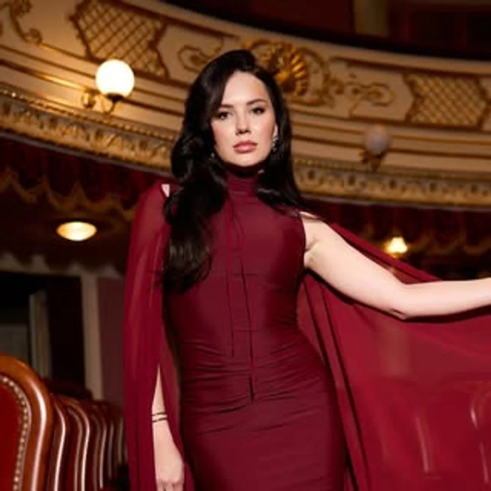 Alina wearing a burgundy cape dress in an ornate theatre interior