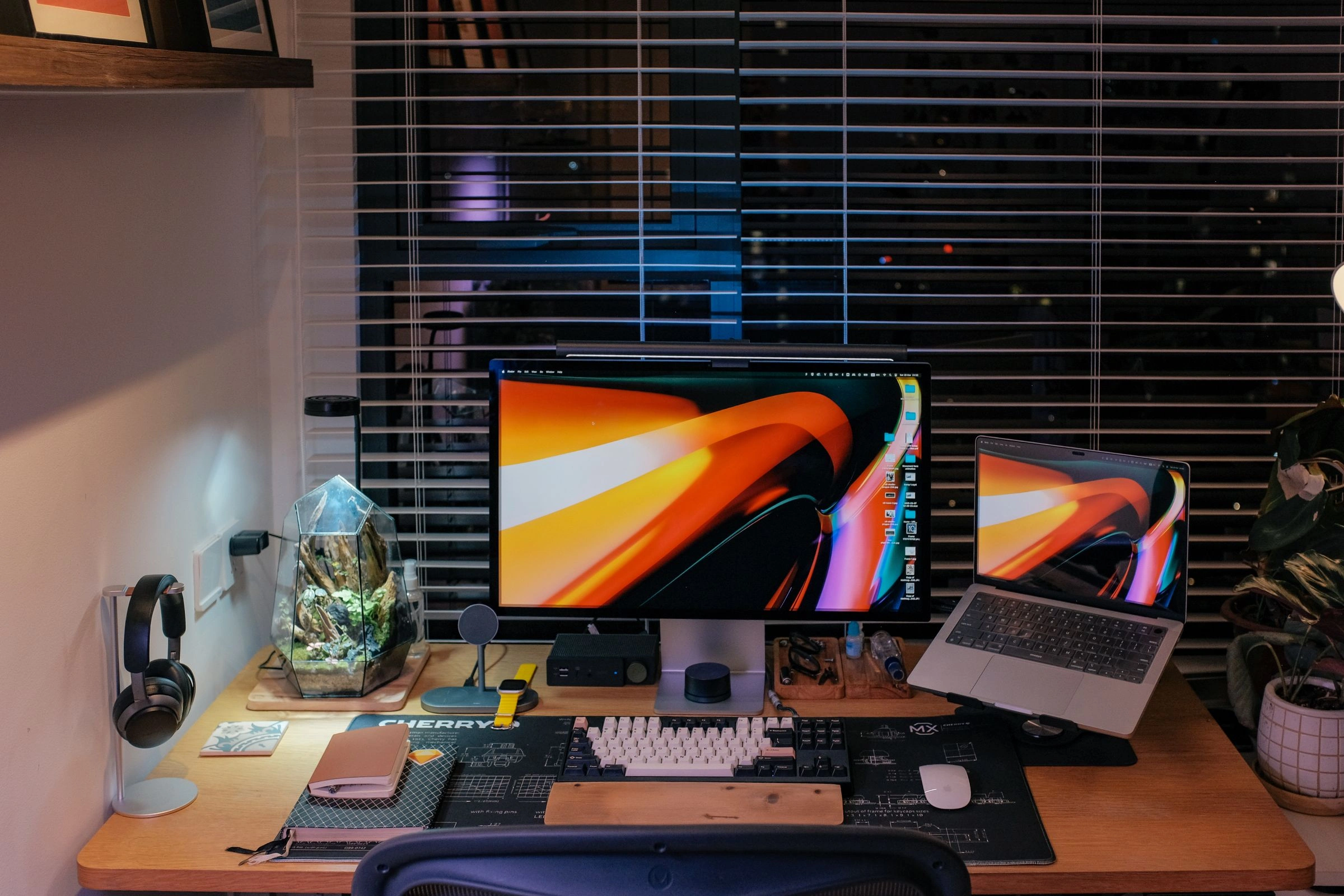 Warm-lit desk setup with a monitor, laptop and mechanical keyboard