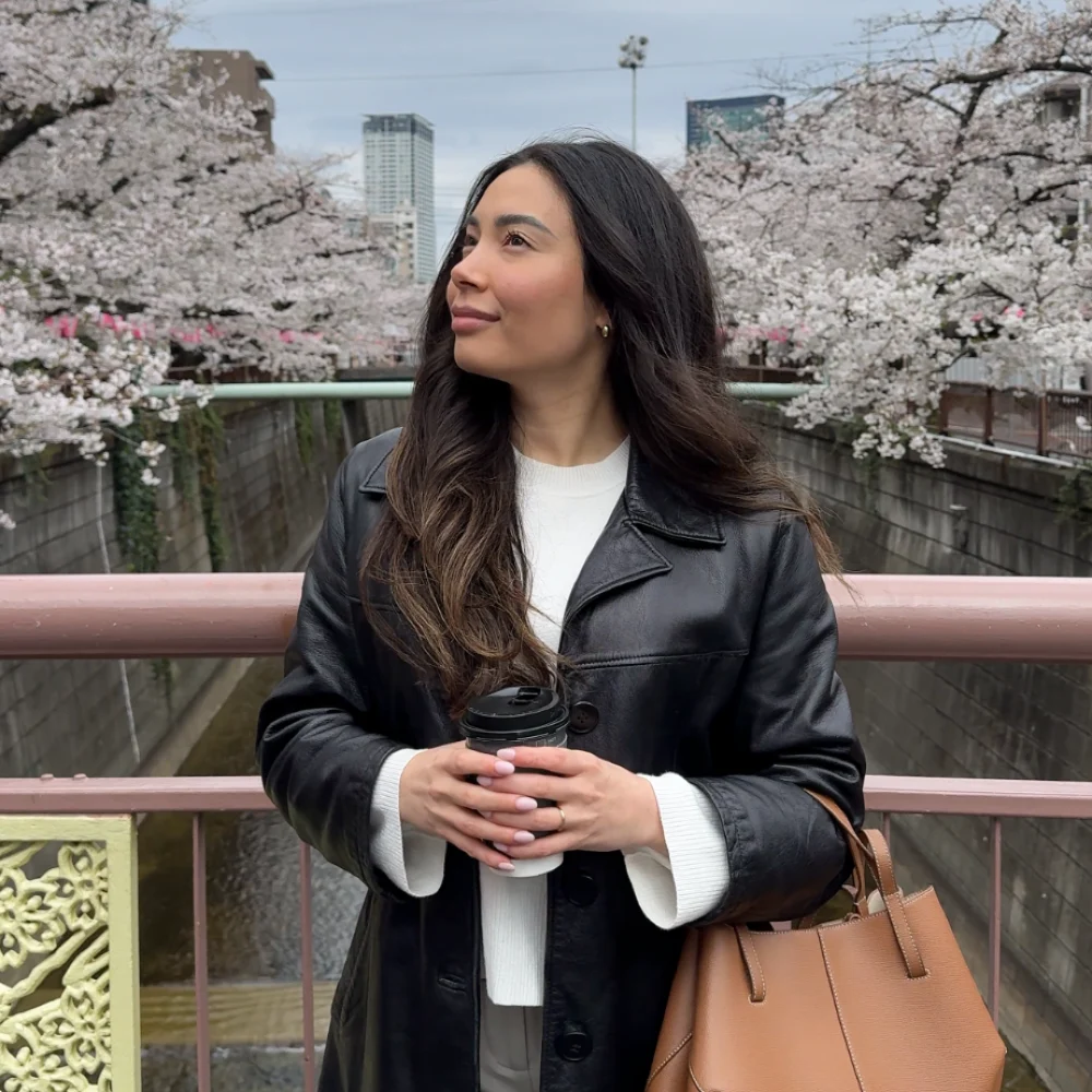 Arabella holding a coffee beside cherry blossoms along a canal