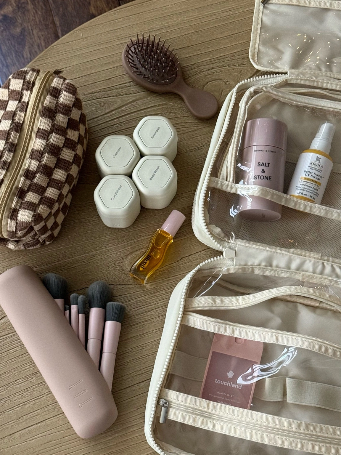 A travel flat lay with a checkered toiletry bag, makeup brushes and skincare