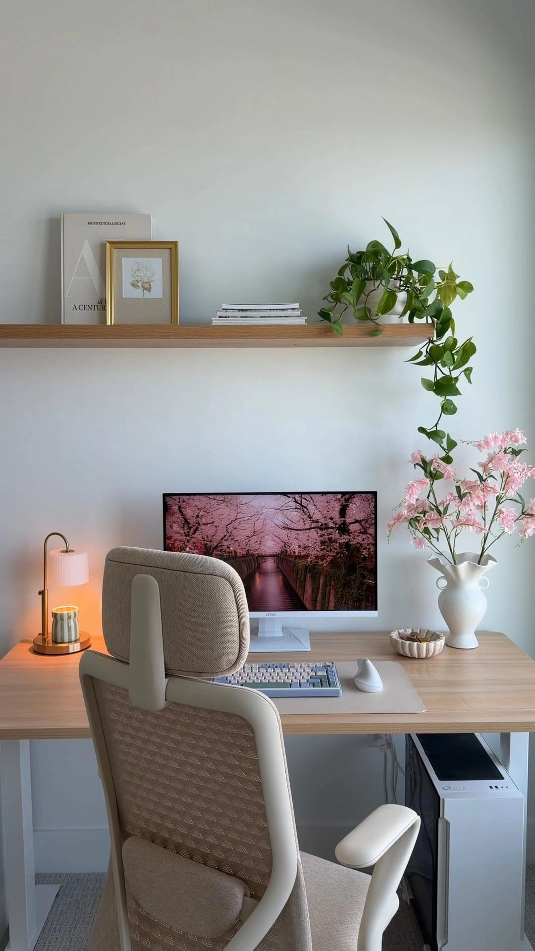 Arabella’s desk with a cream chair, glowing lamp, monitor and pink blossoms