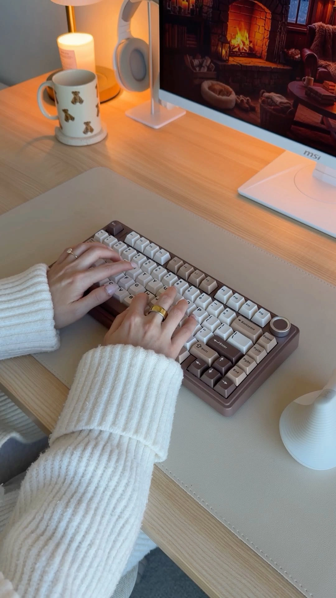 Hands in a knit sweater typing beside a teddy bear mug and candle