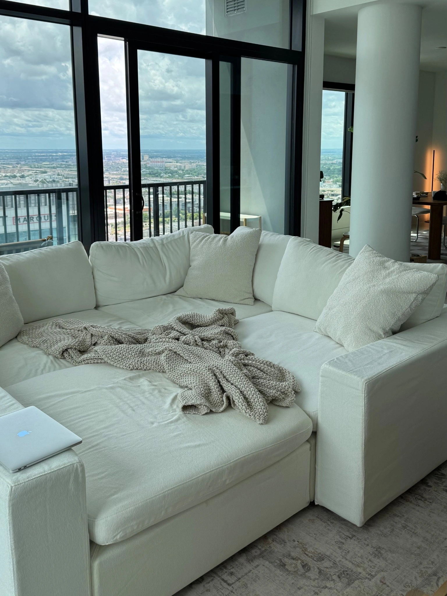 A cream modular sofa with a knit throw beside tall windows