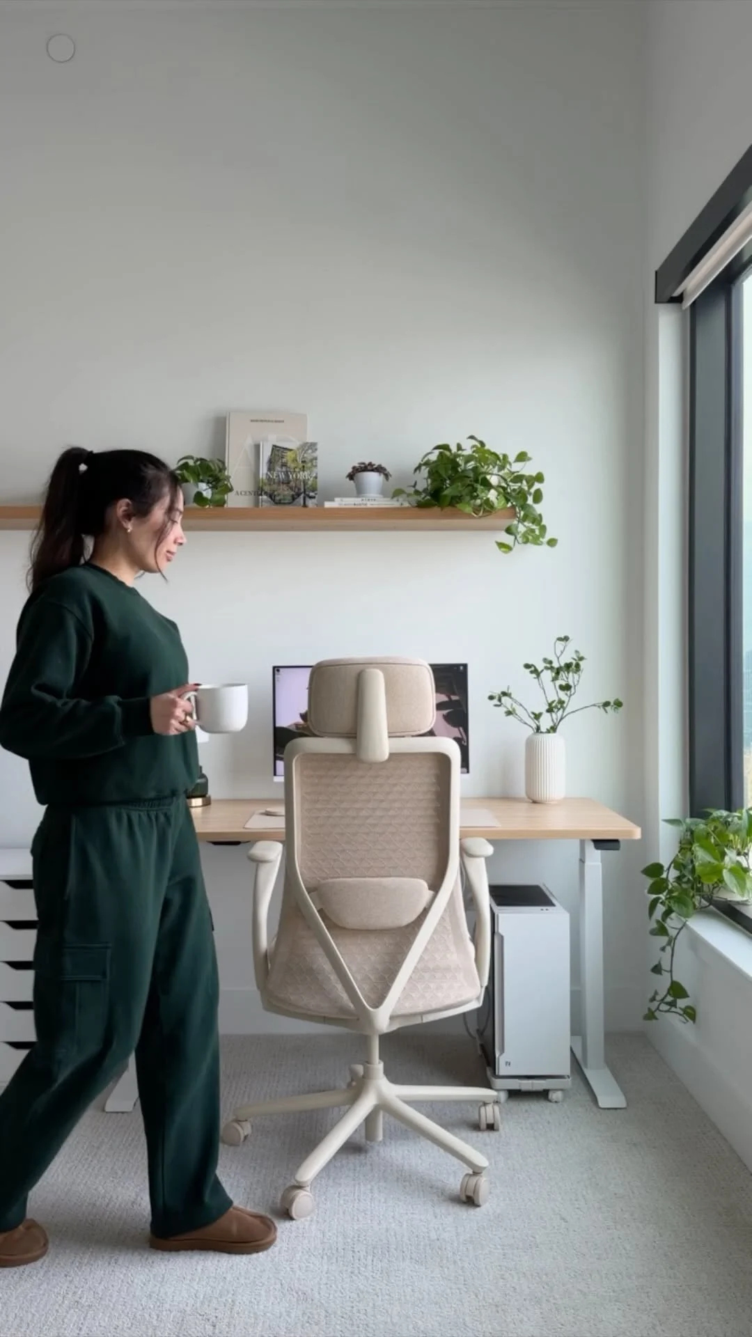 Arabella in a green sweatsuit carrying a mug past her desk