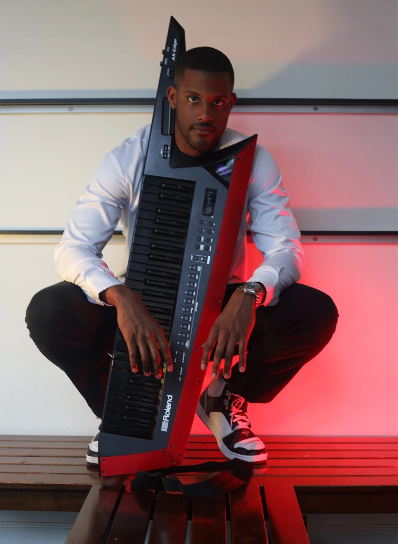 Chops crouching with a Roland keytar against a red-lit wall