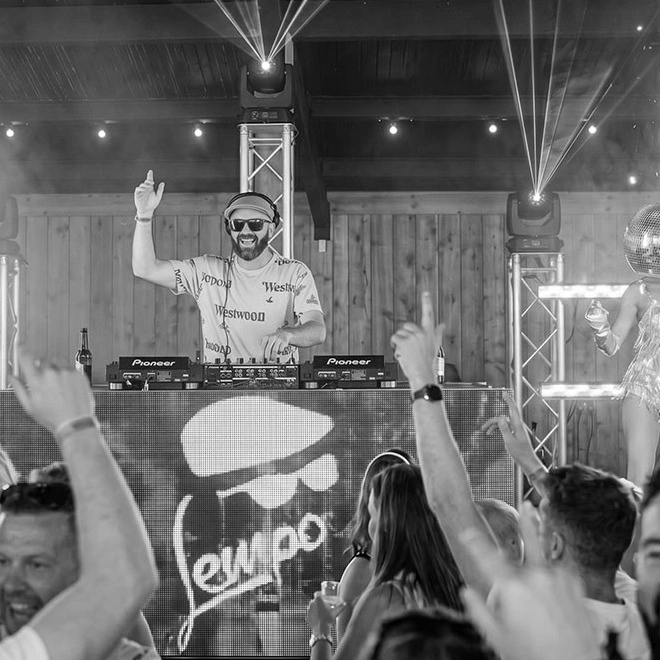 A crowd with hands up in front of a DJ booth carrying the Lempo logo