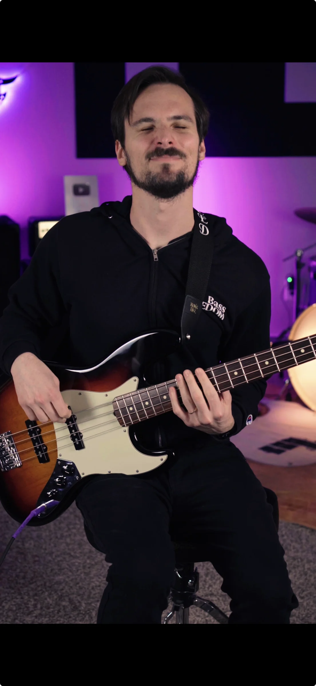 Andrew Freed seated in his studio holding a bass guitar