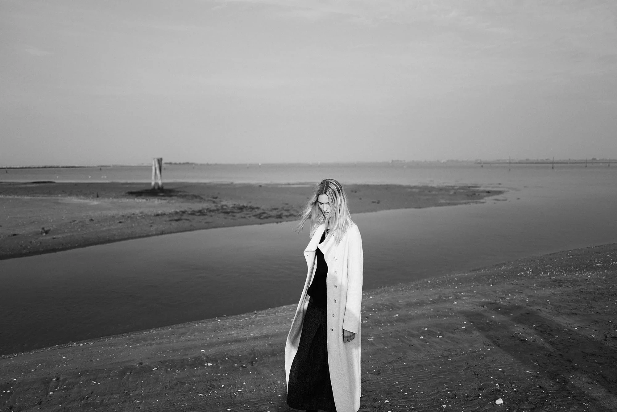 Una donna in cappotto bianco su una spiaggia grigia