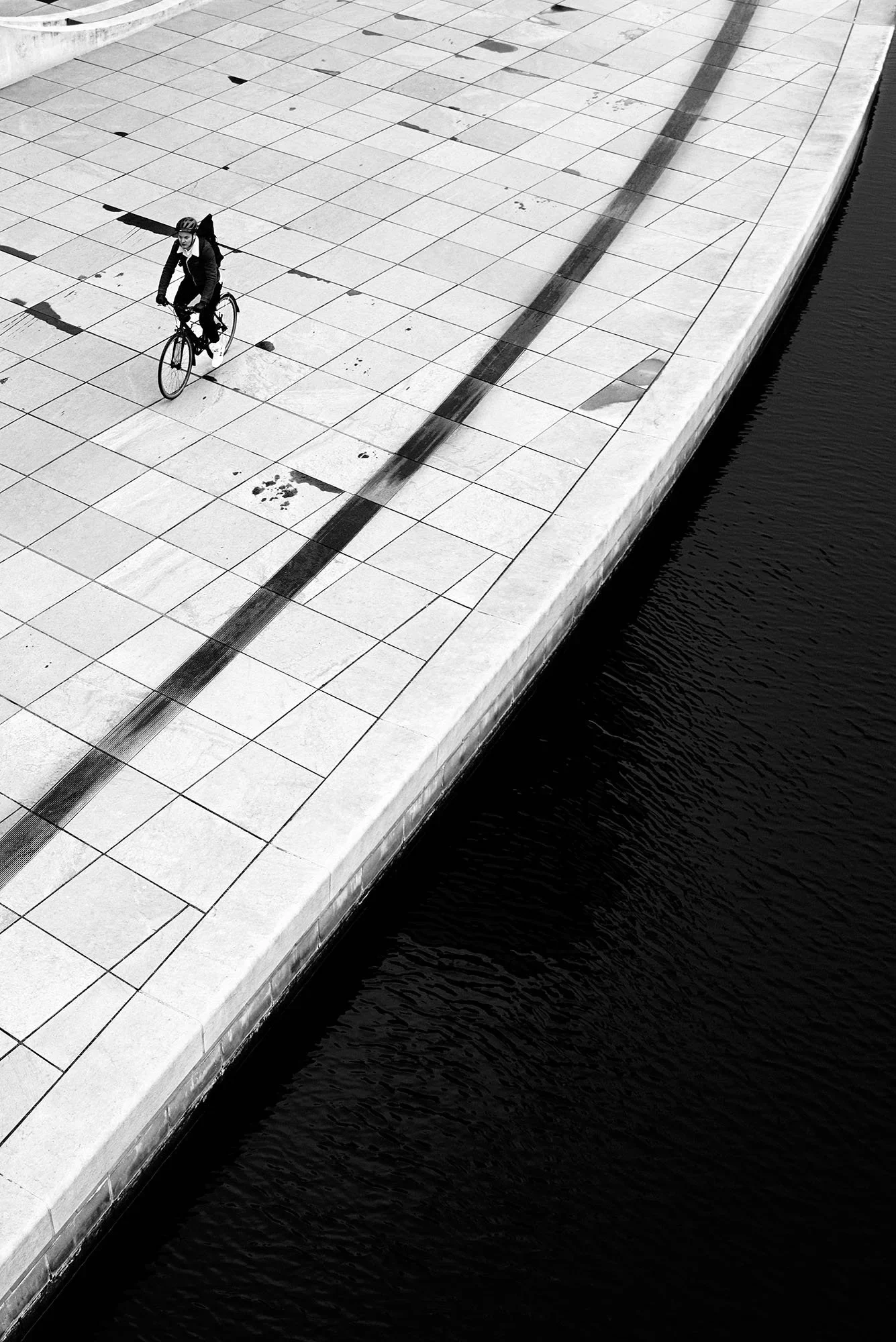 Un ciclista su una piazza lastricata che curva sopra l’acqua scura