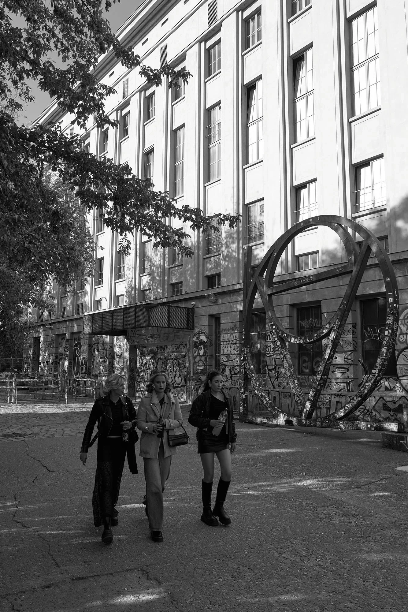 Tre donne camminano su un viale davanti a un edificio e a una scultura ad anelli