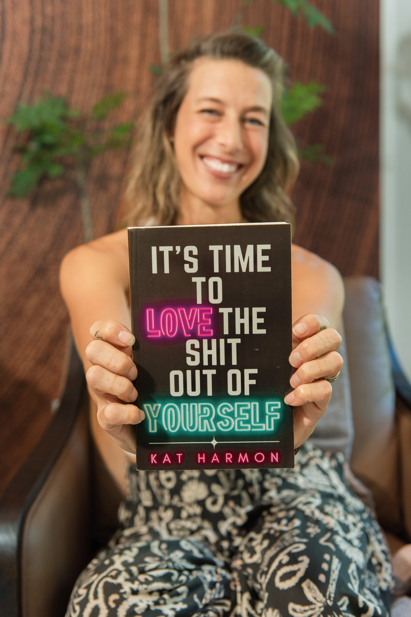 Kat holding her book It’s Time to Love the Shit out of Yourself