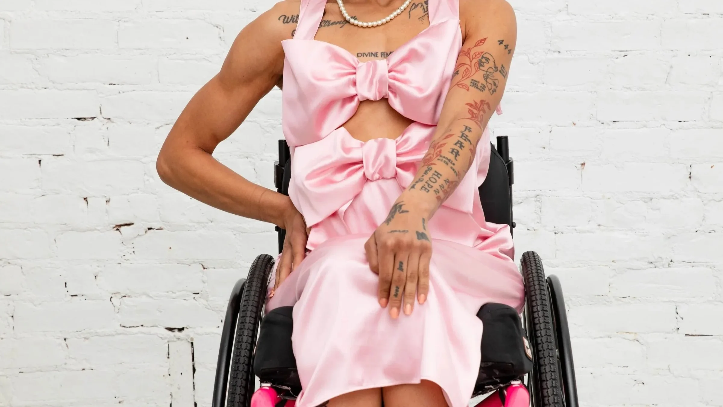 Model seated in a wheelchair wearing the pink Signed Mya statement bow dress