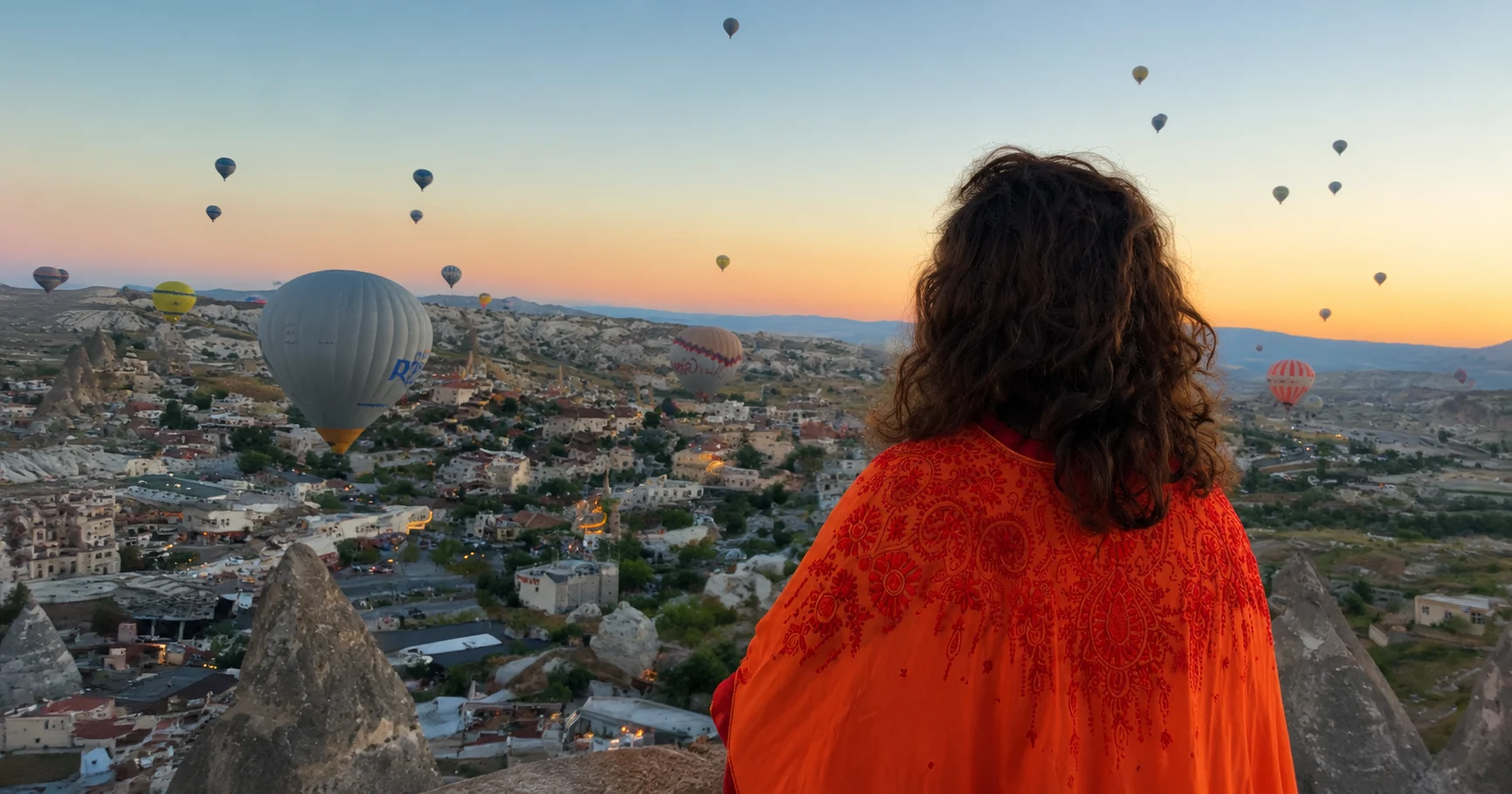 A woman looking across Cappadocia as hot-air balloons rise at sunrise