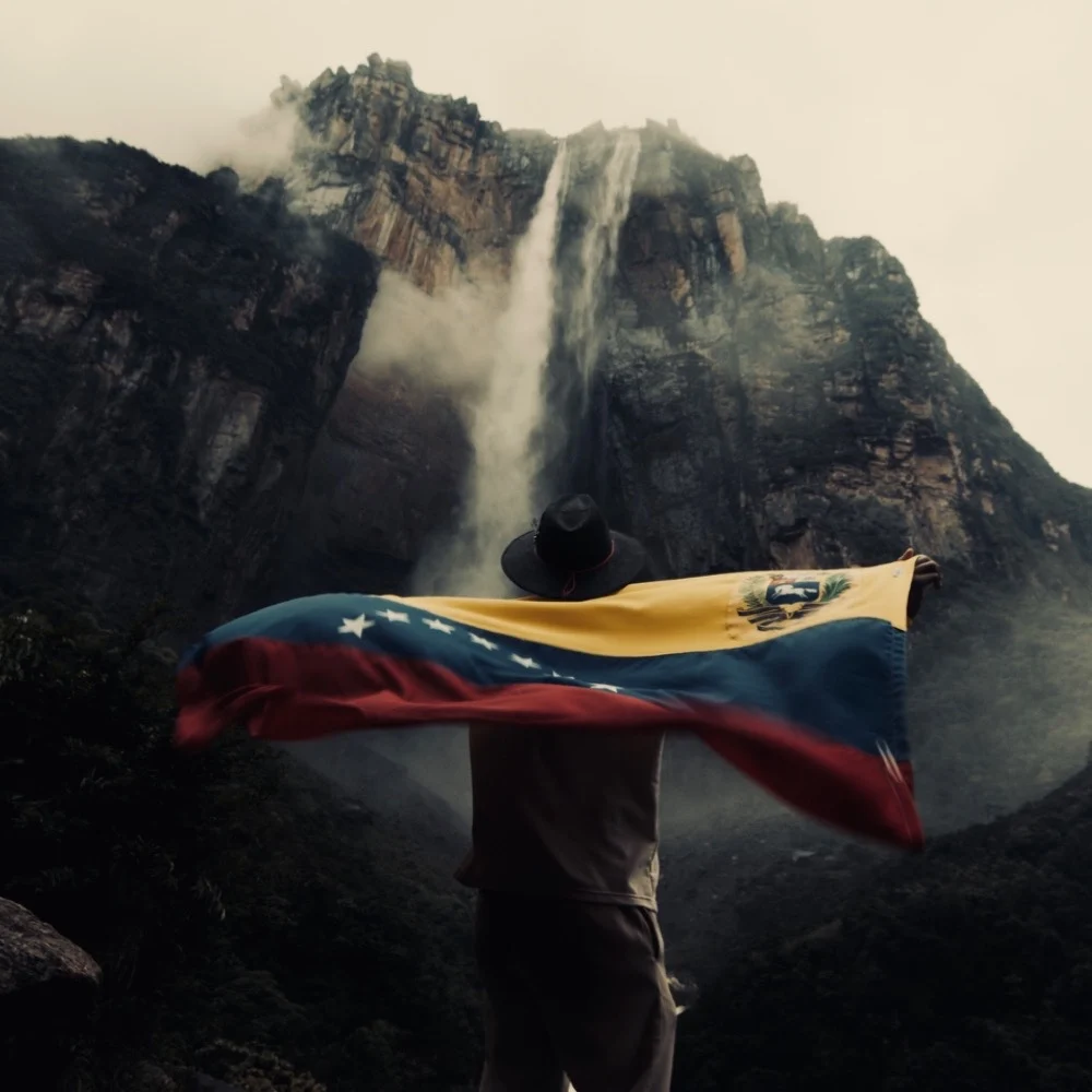 Viajero sosteniendo la bandera de Venezuela frente a una cascada
