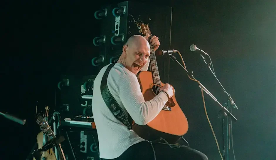 Fin Furey smiling with an acoustic guitar during a live performance