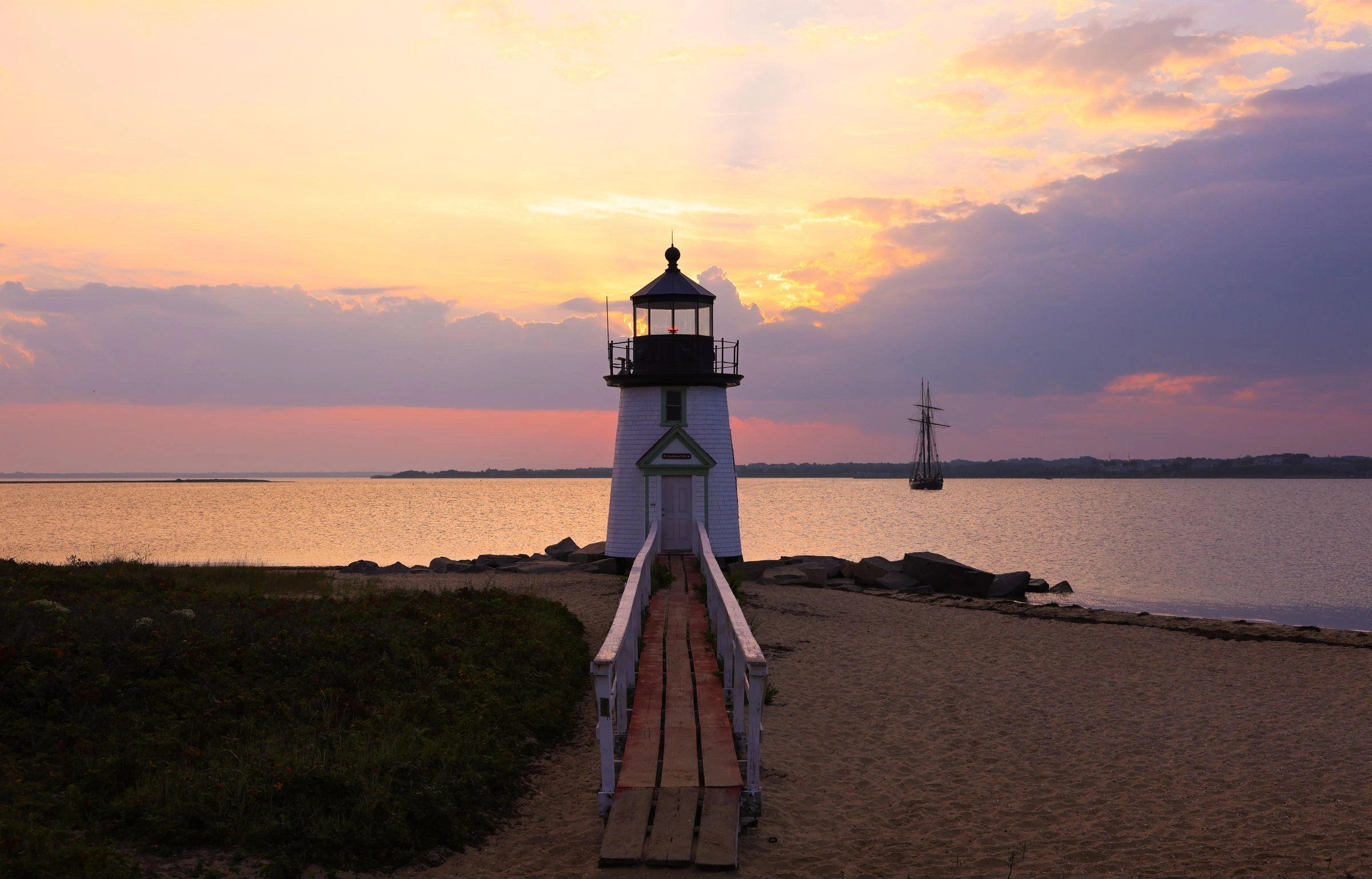 White lighthouse at the end of a boardwalk under a pink and lavender sunset