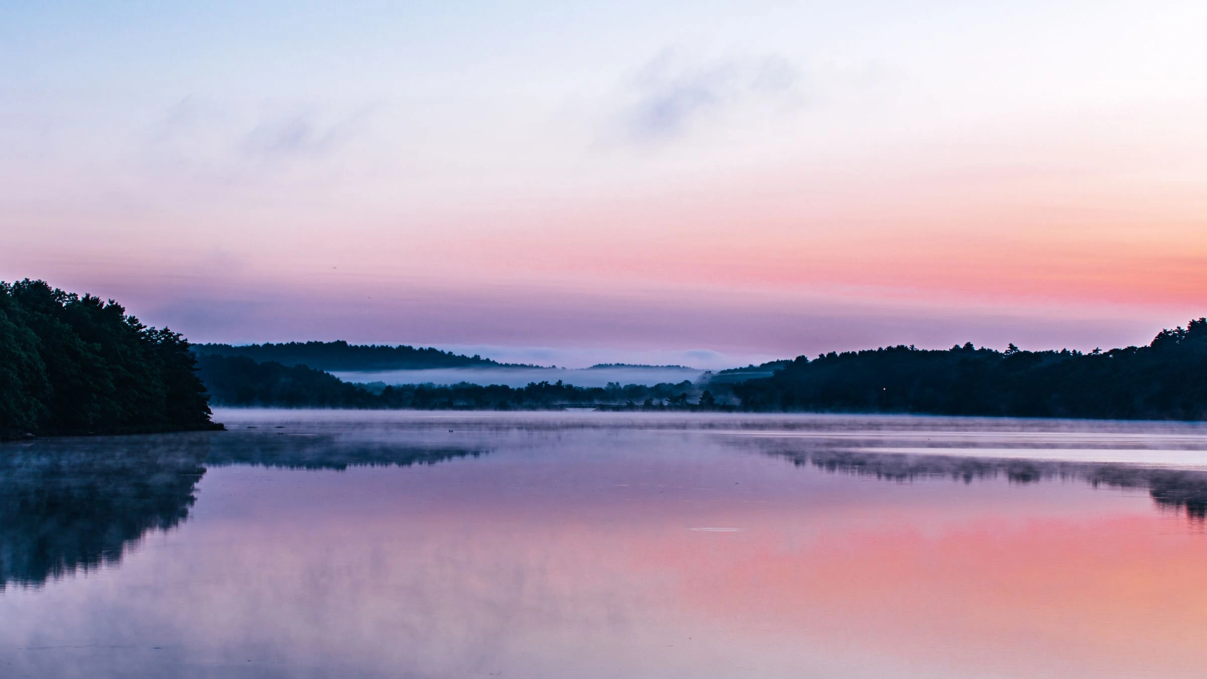 Misty lake at sunrise under a pastel pink sky