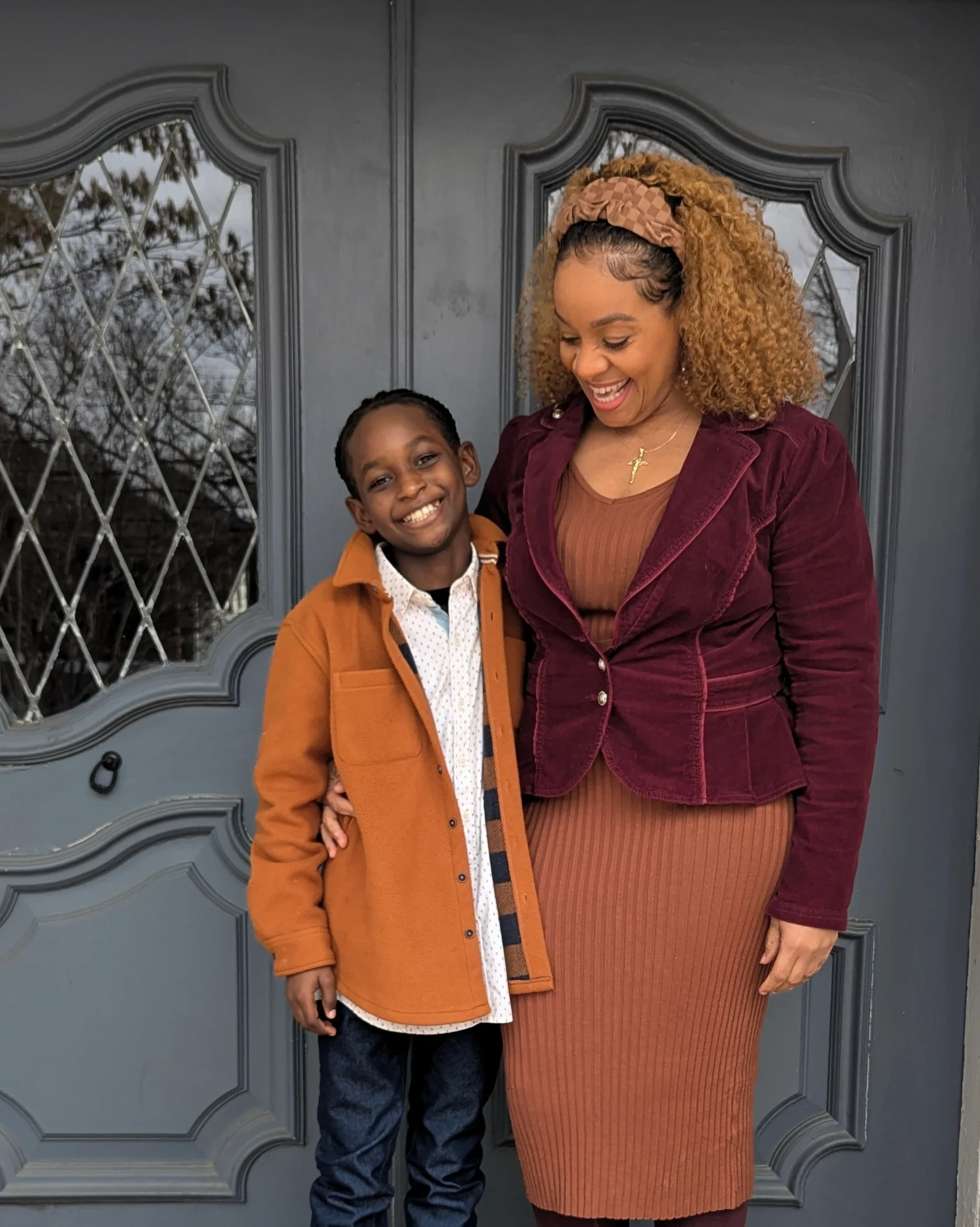 A mother and her young son smiling at their front door