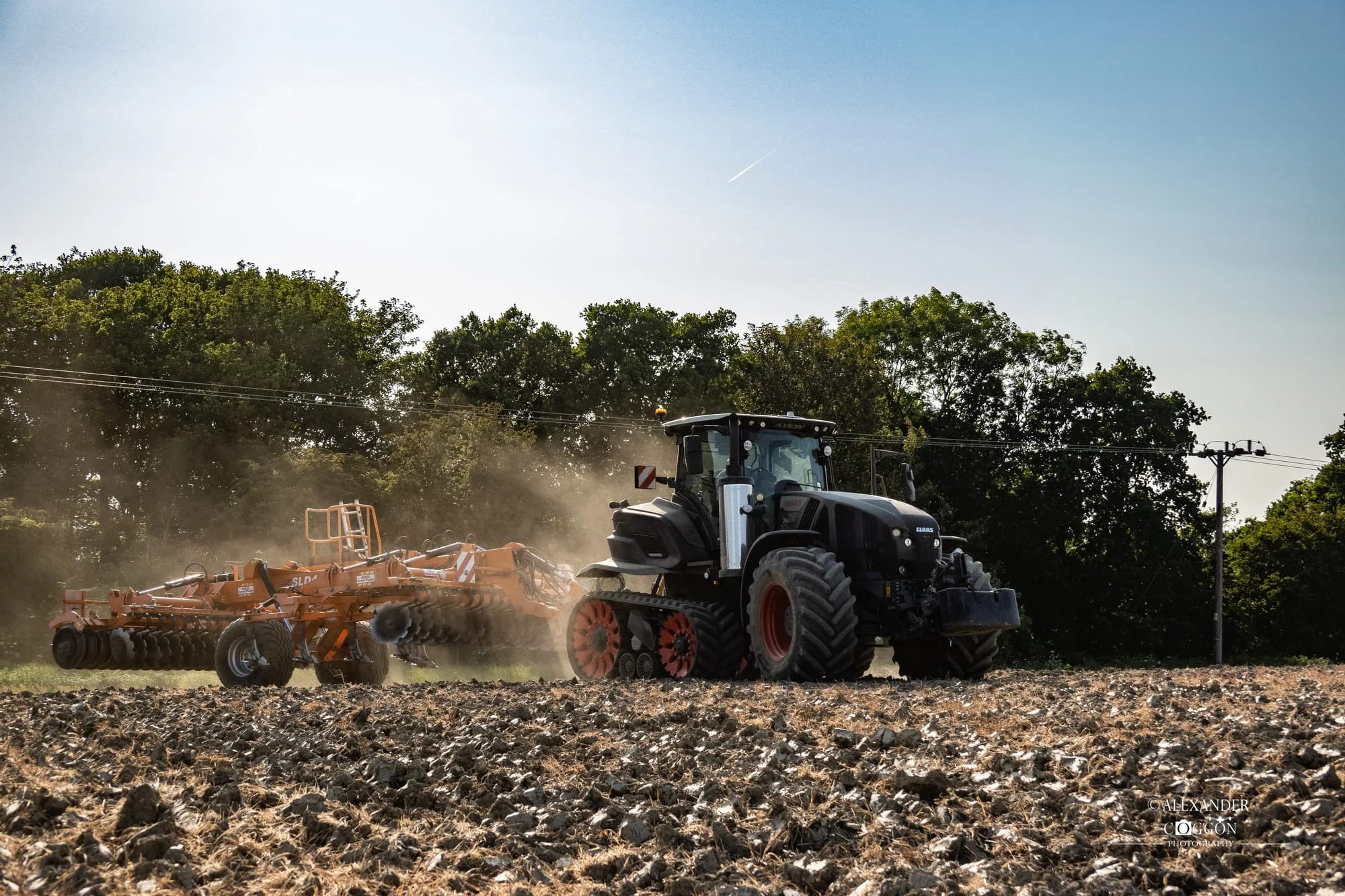 Tractor working a dusty field beside trees