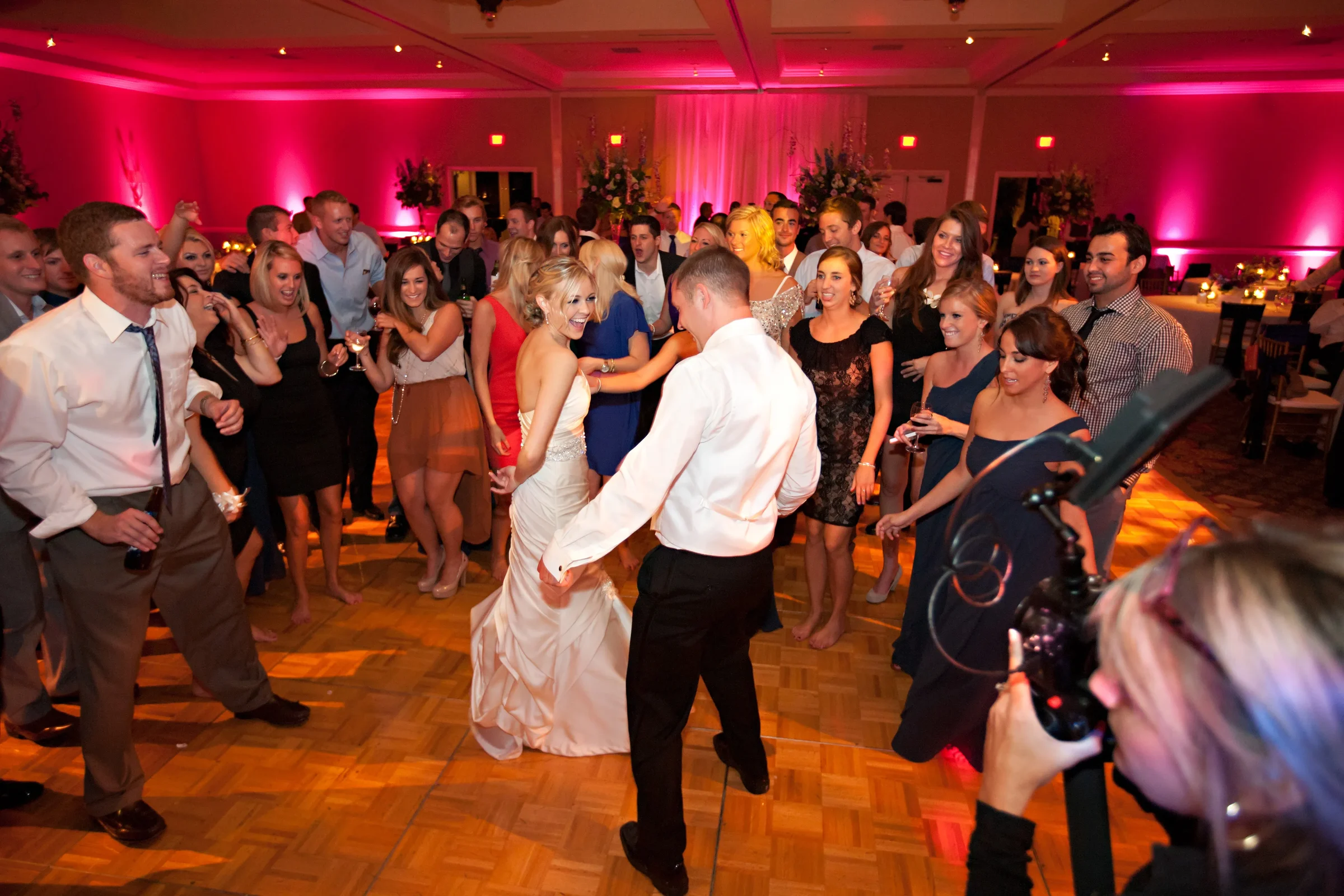 A packed wedding dance floor under vivid pink lights