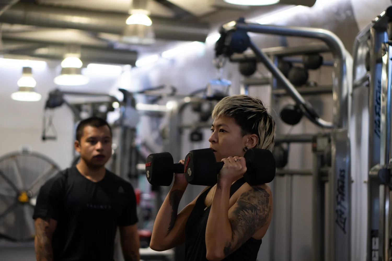 Marwin coaching a client through a dumbbell exercise in the gym