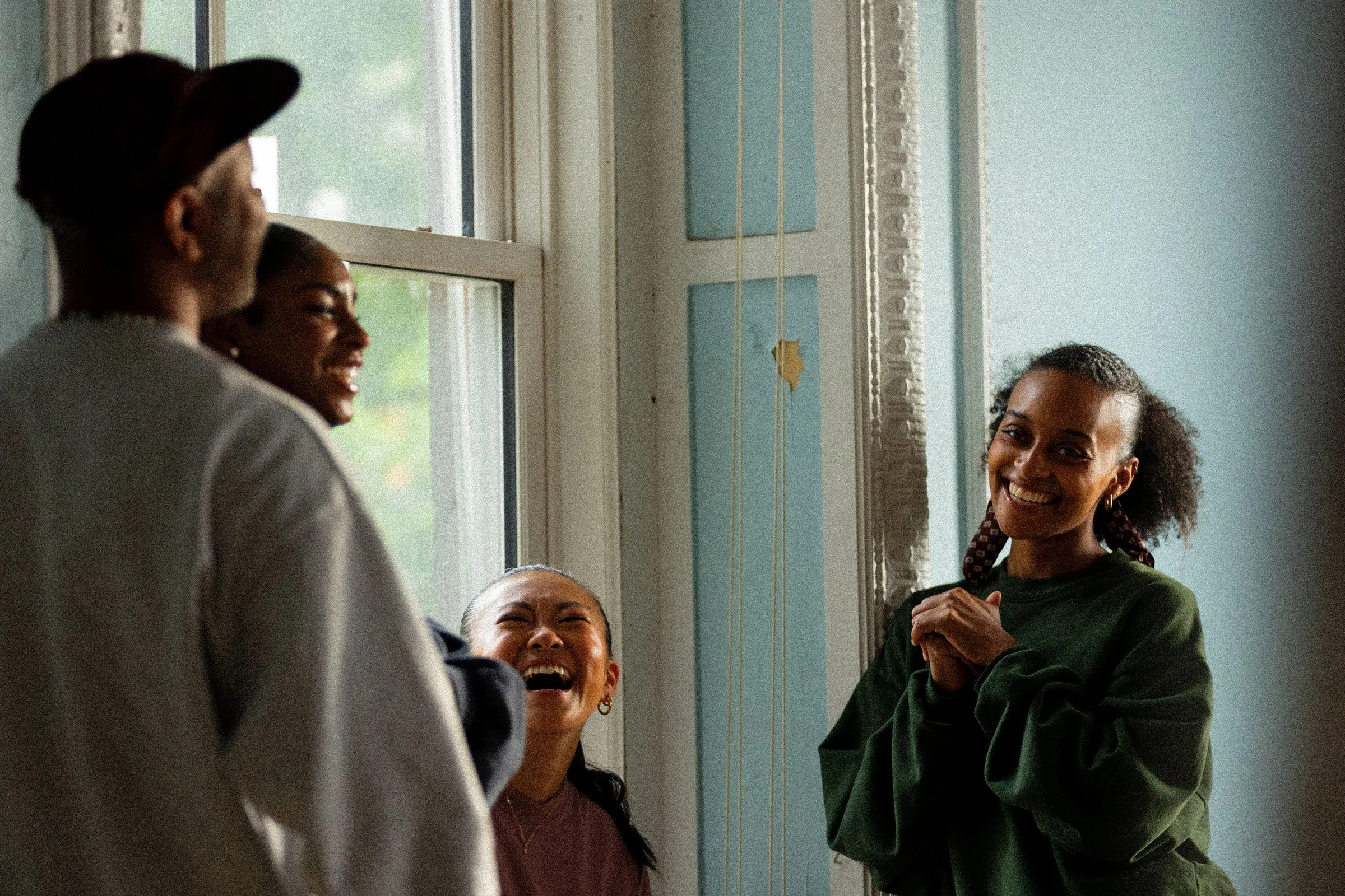 Four dancers laughing together in a sunlit studio