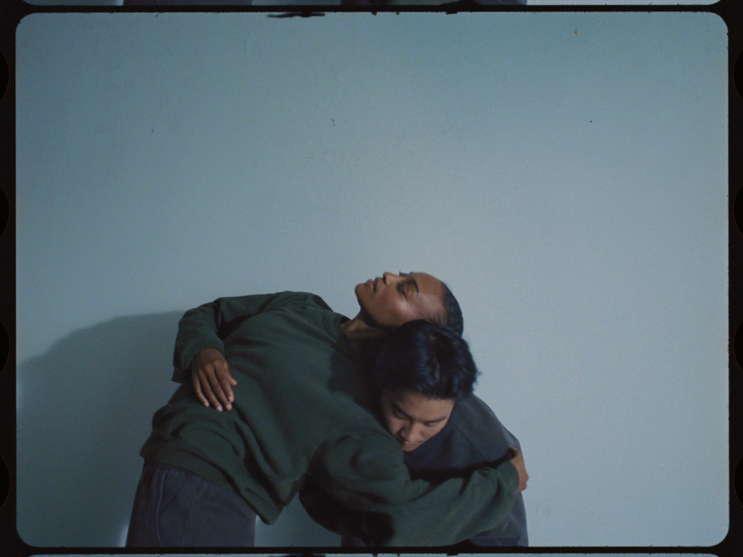 Two dancers embracing with heads tilted back against a pale wall