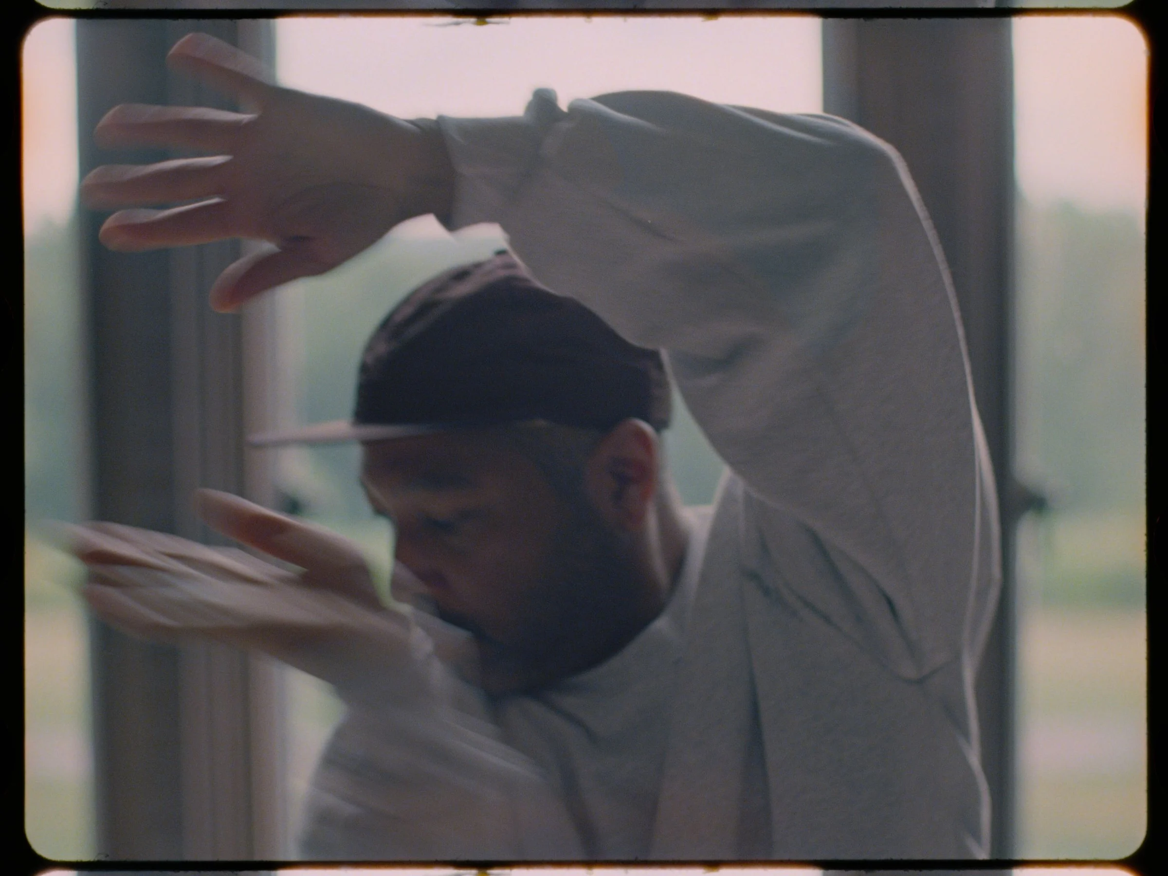 Kyle Abraham mid-motion with both arms extended in front of a window