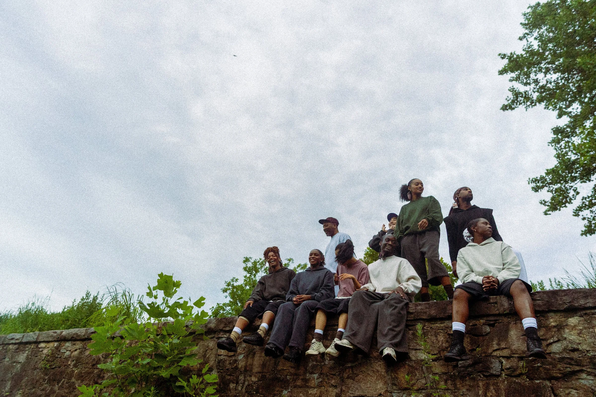 The company sitting and standing on a stone wall under an overcast sky