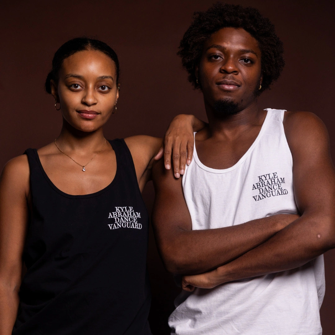 Two dancers wearing black and white tanks with the Kyle Abraham Dance Vanguard wordmark