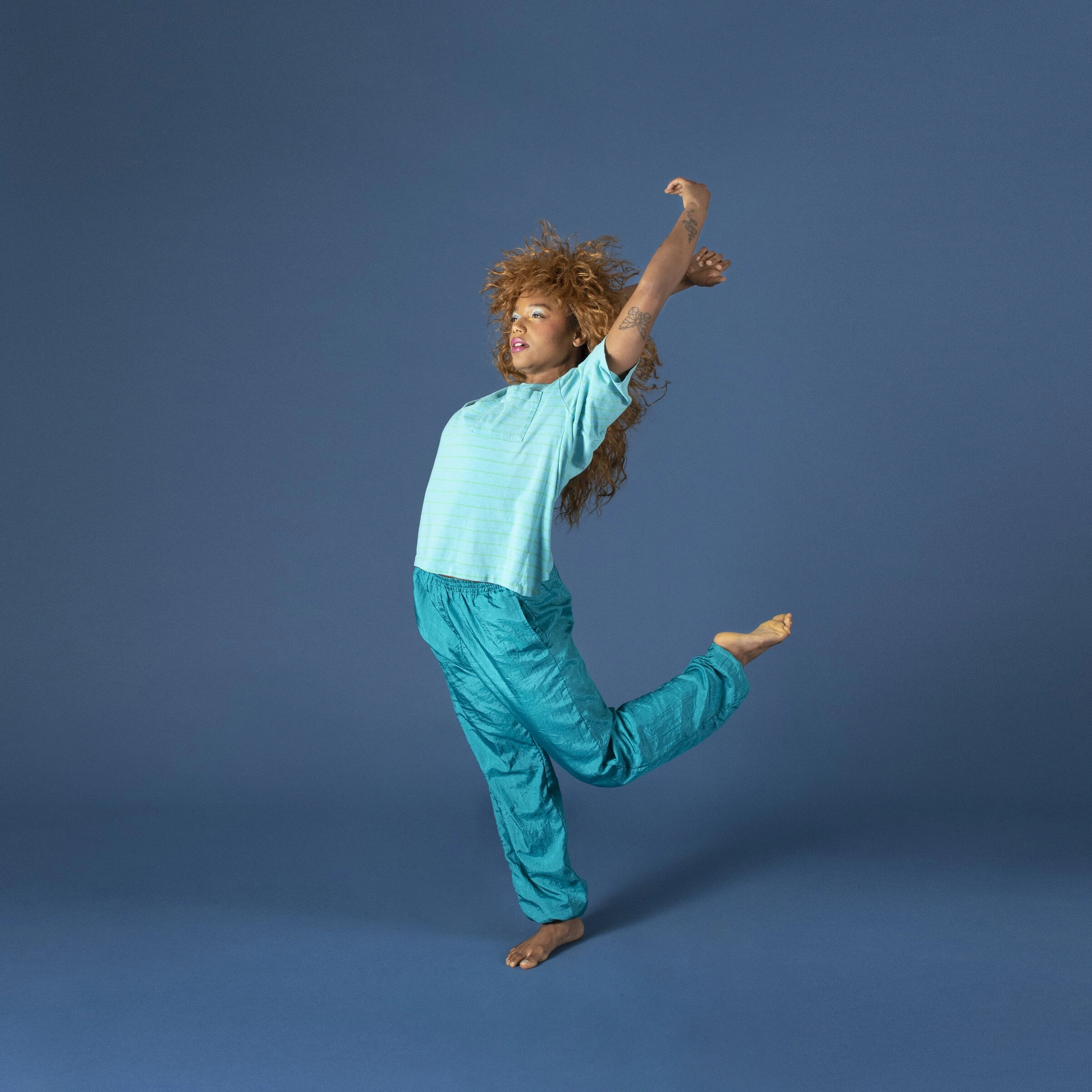 Gianna Theodore leaping in a teal windbreaker outfit against a blue backdrop in Cassette Vol. 1