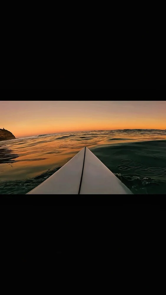 Point-of-view surfboard entering the ocean at sunrise