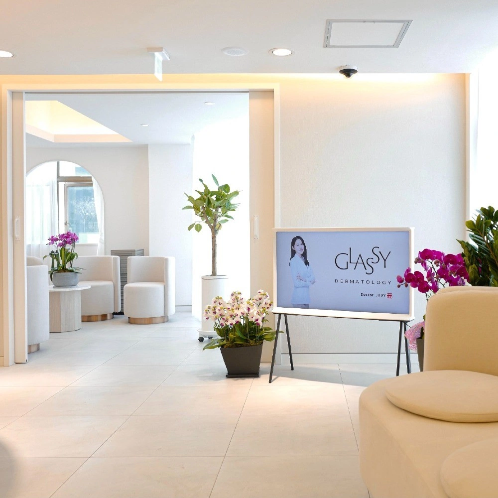 Bright cream lounge at Glassy Skin Clinic with armchairs, orchids and a GLASSY Dermatology screen