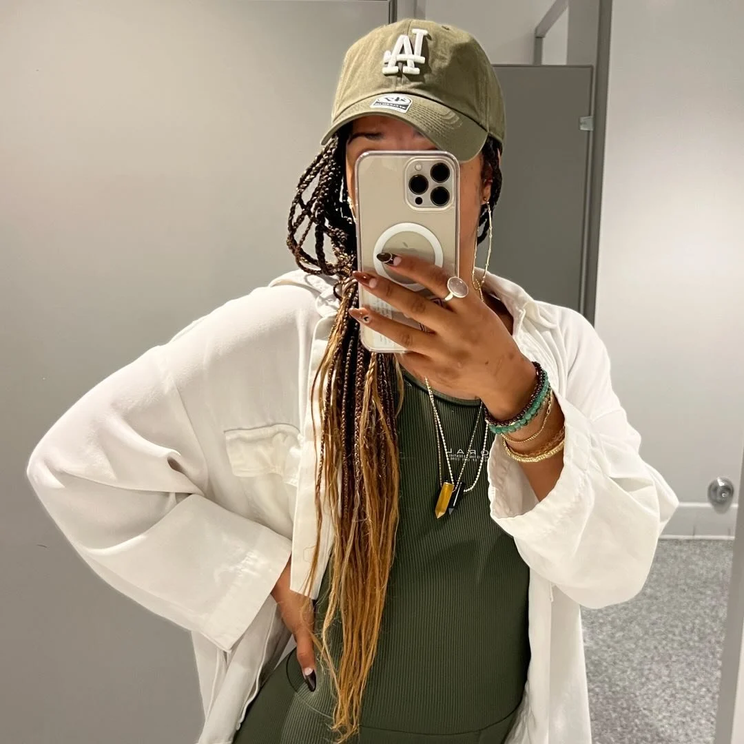 TOSH taking a mirror selfie in a green cap and layered neutral outfit