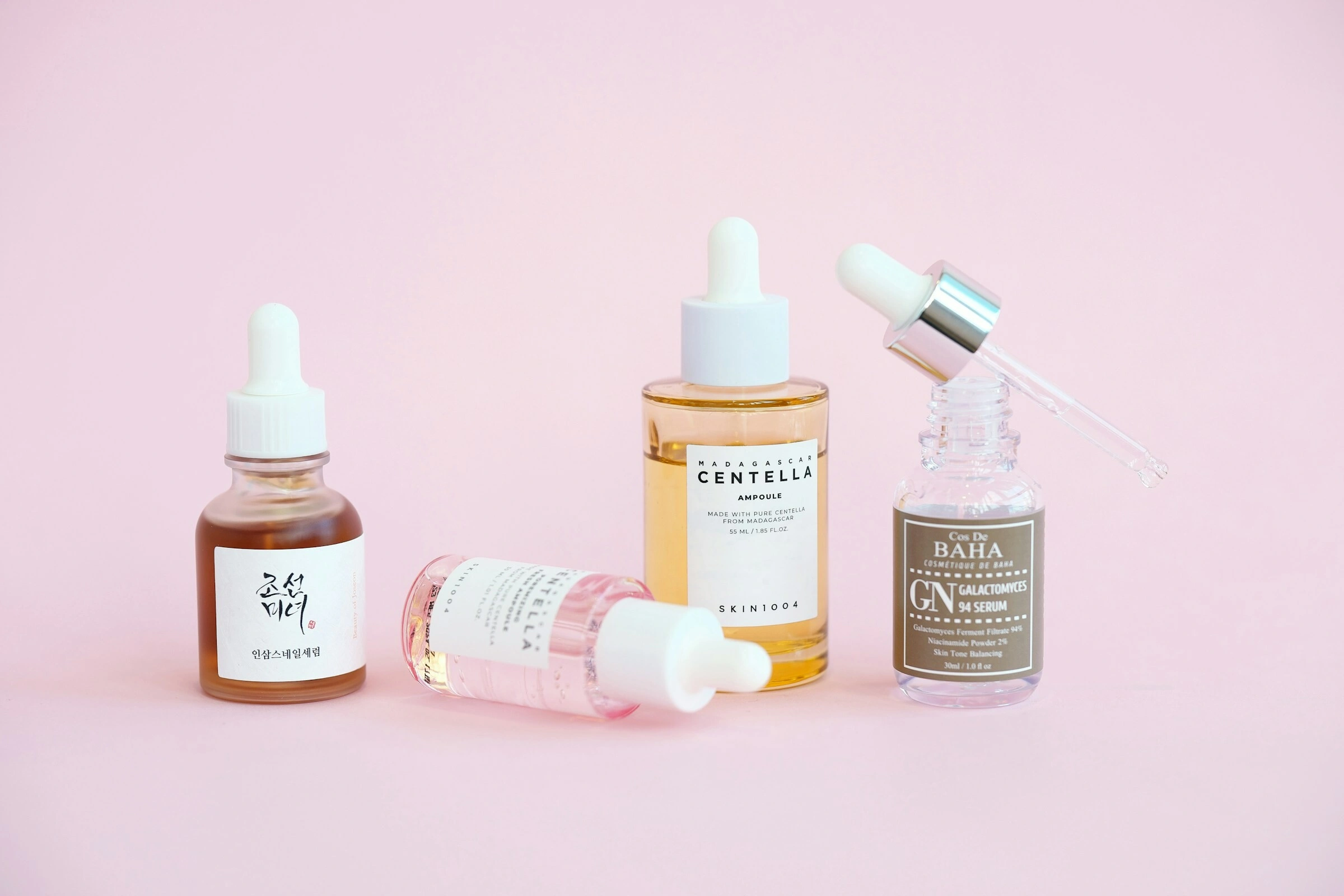 Skincare serums and dropper bottles on a pink background