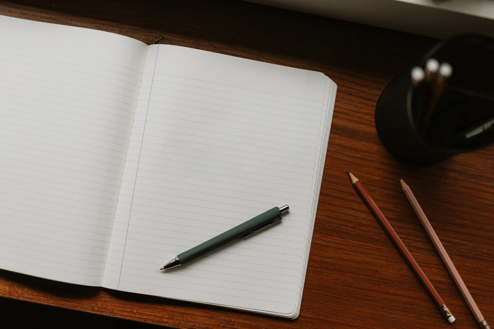 Open blank notebook with a pen and pencils on a wooden desk