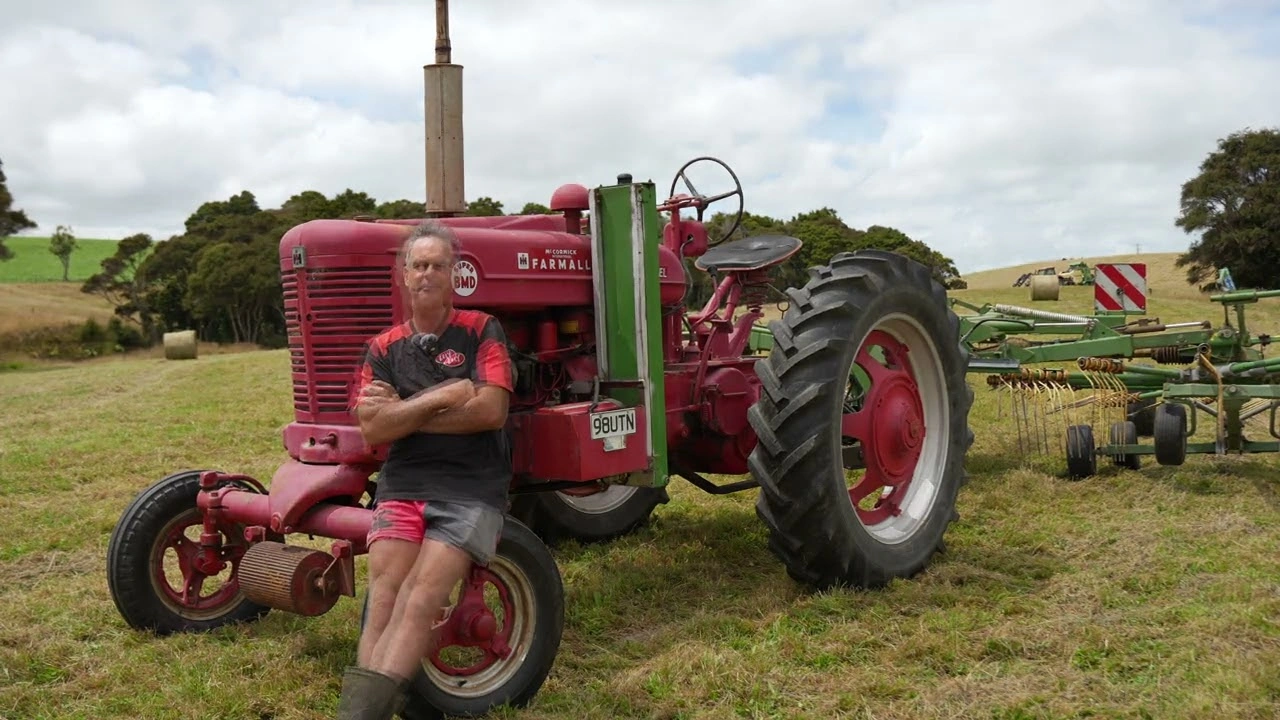Farmer Gregg Gemmell leaning on a red vintage tractor in a New Zealand hay field