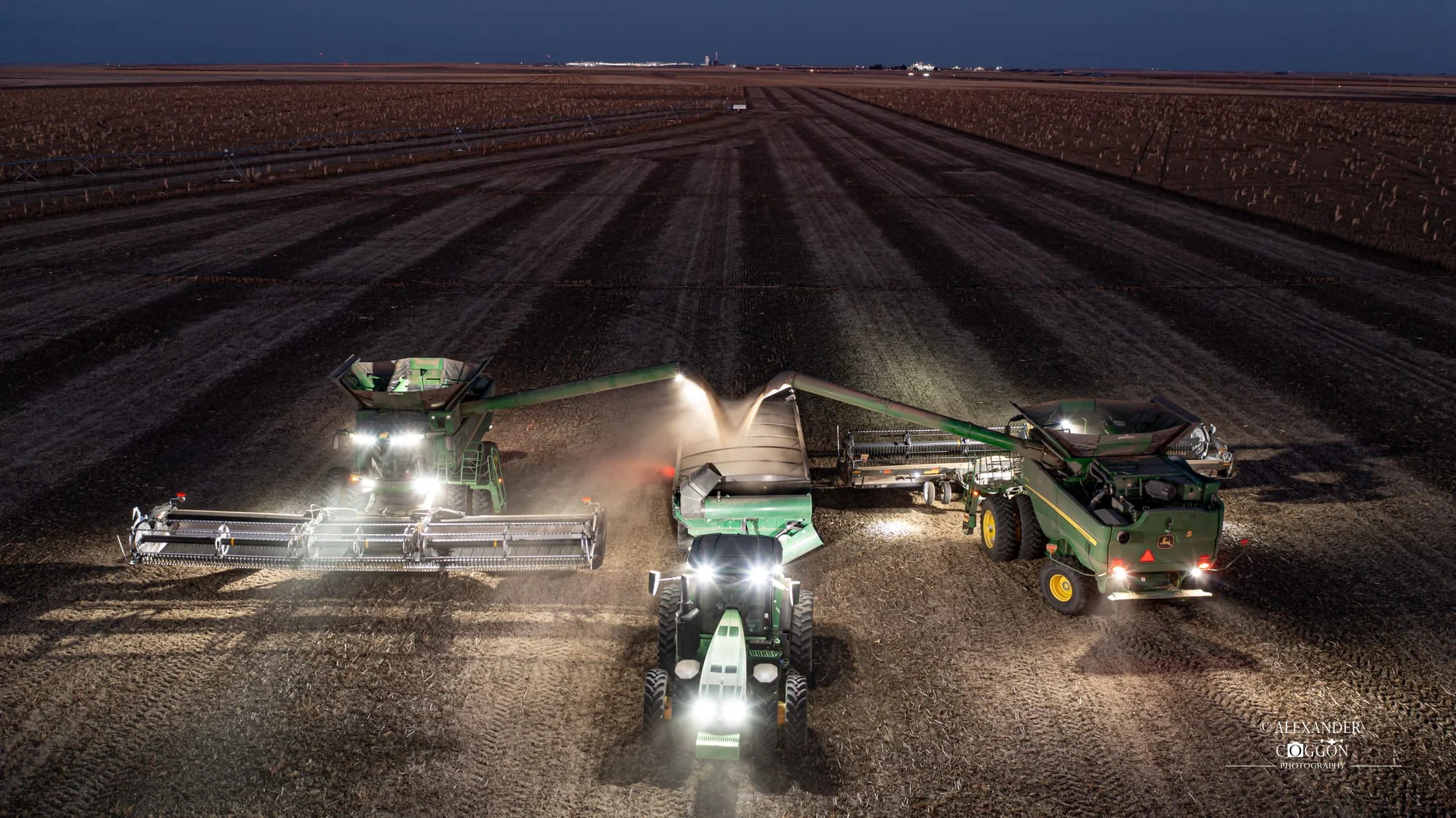 Combine and trailers working under lights at night