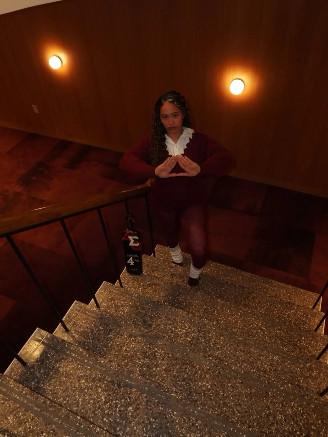 Kennedy Aniyah in a crimson sweater making a hand sign at the top of a stairwell