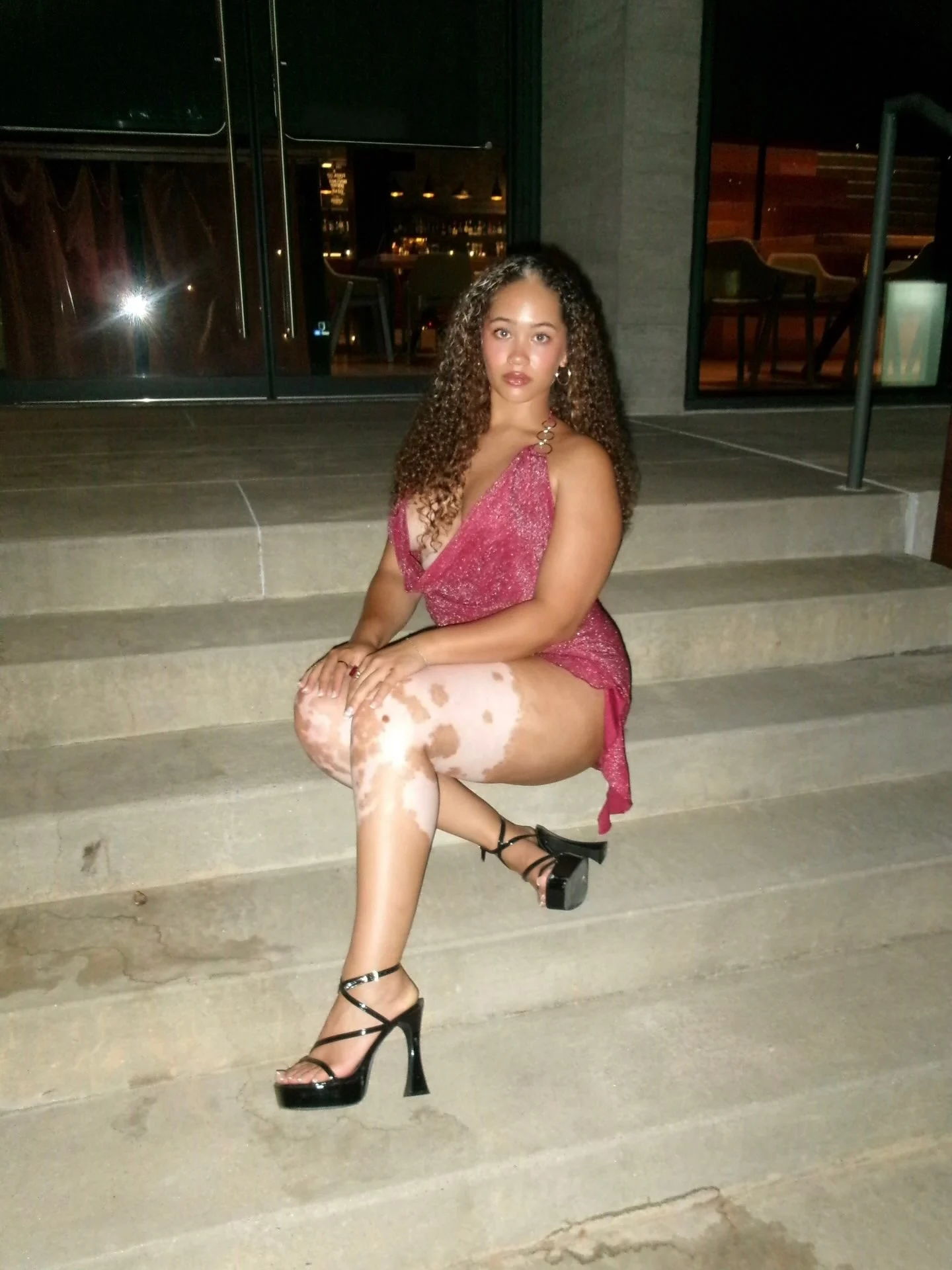 Kennedy Aniyah in a pink sequin dress and strappy heels sitting on concrete steps at night