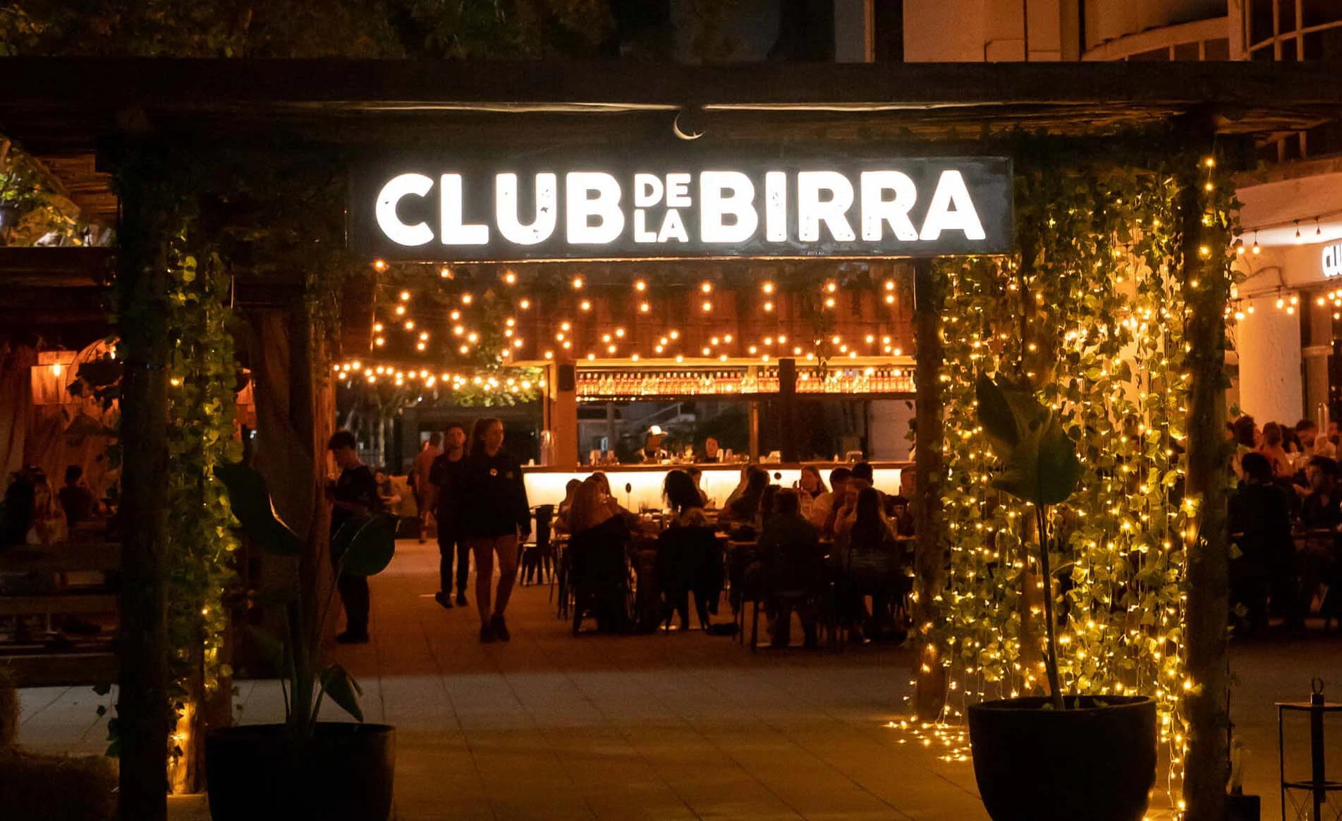 Entrada iluminada del Club de la Birra con gente reunida de noche
