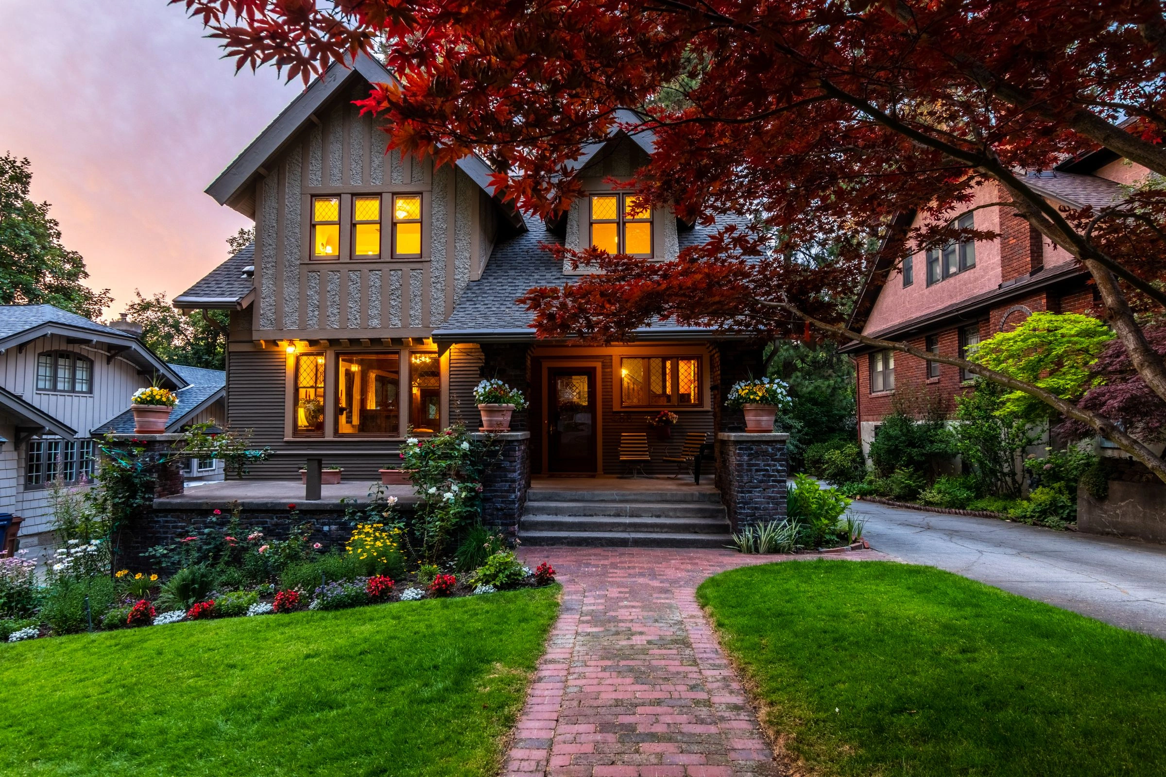 Craftsman home at dusk with glowing windows, a red Japanese maple and a brick path across the lawn