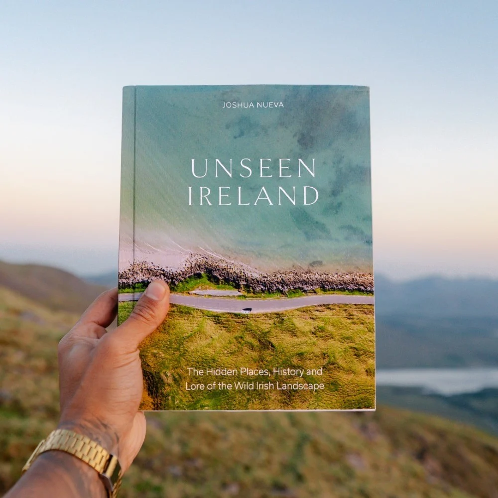 Unseen Ireland photography book held above a rugged Irish landscape
