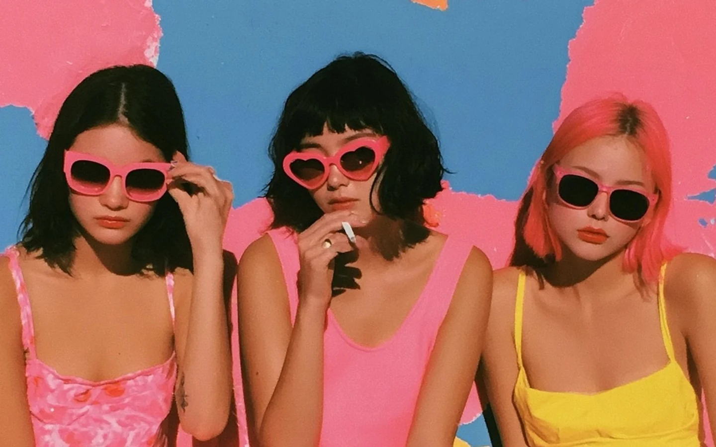 Three people wearing pink sunglasses in different shapes against a pink and blue background