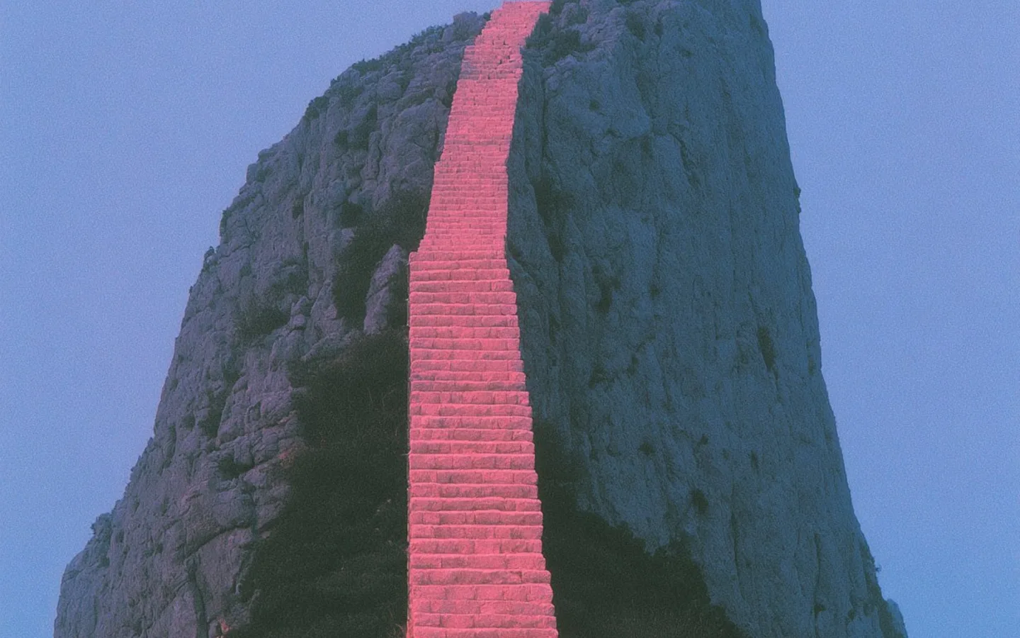A long pink stairway climbing the face of a blue cliff