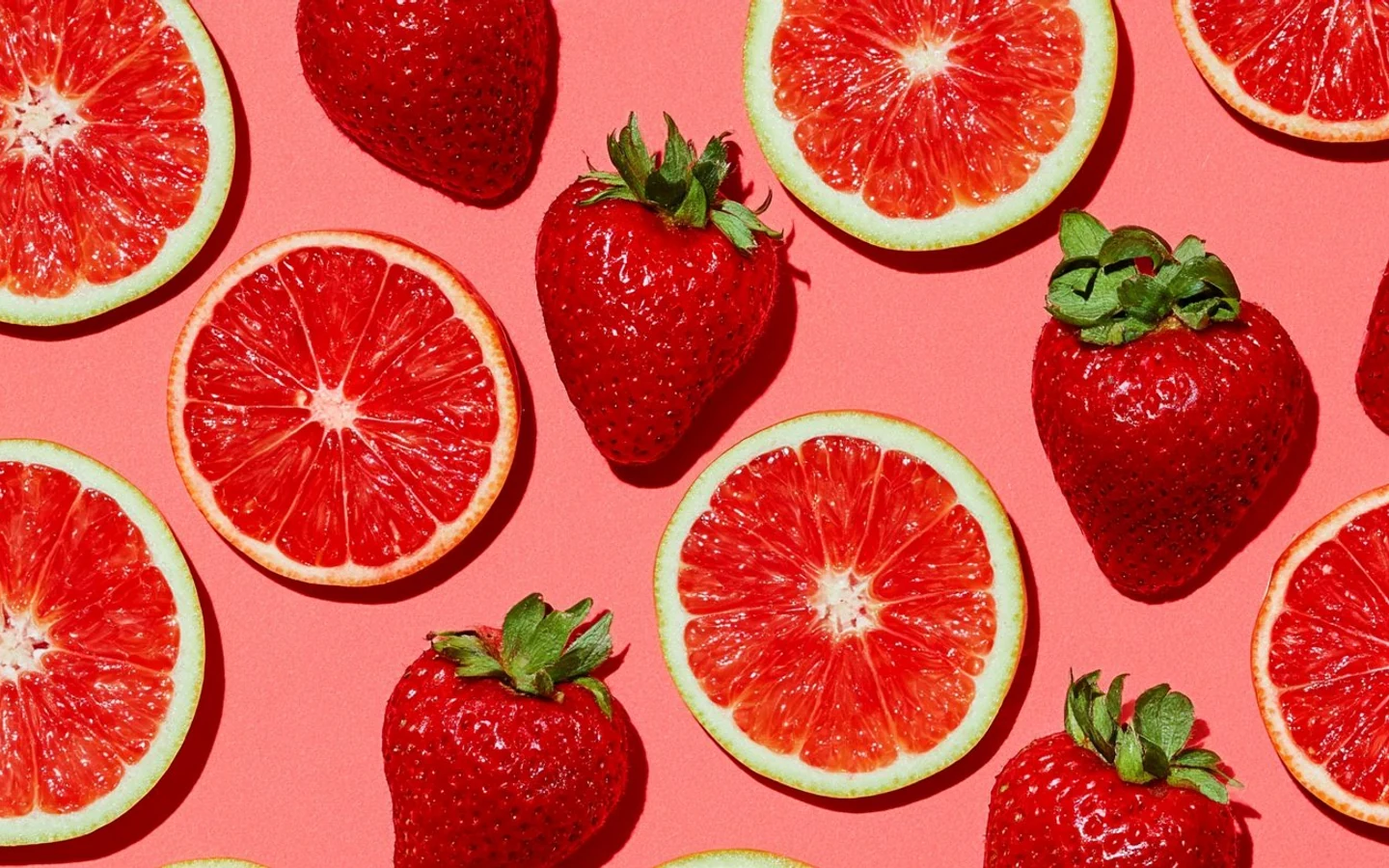 Strawberries and slices of pink grapefruit arranged on a coral background